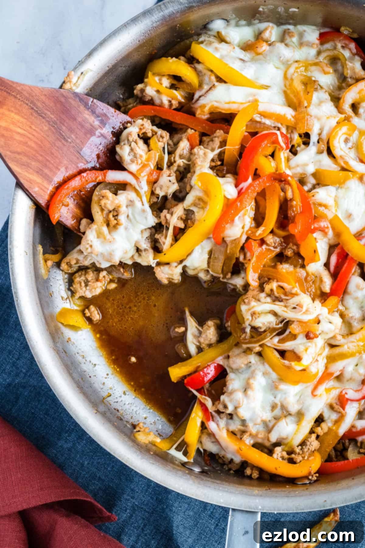 A finished Chicken Cheesesteak Skillet with melted cheese, with a wooden spoon scooping out a serving.