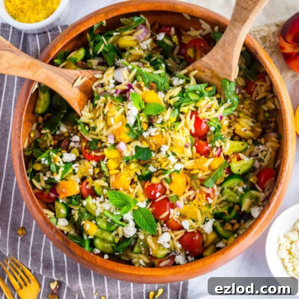 Colorful summer orzo salad with peaches, cherry tomatoes, cucumbers, and feta served in a large white bowl.