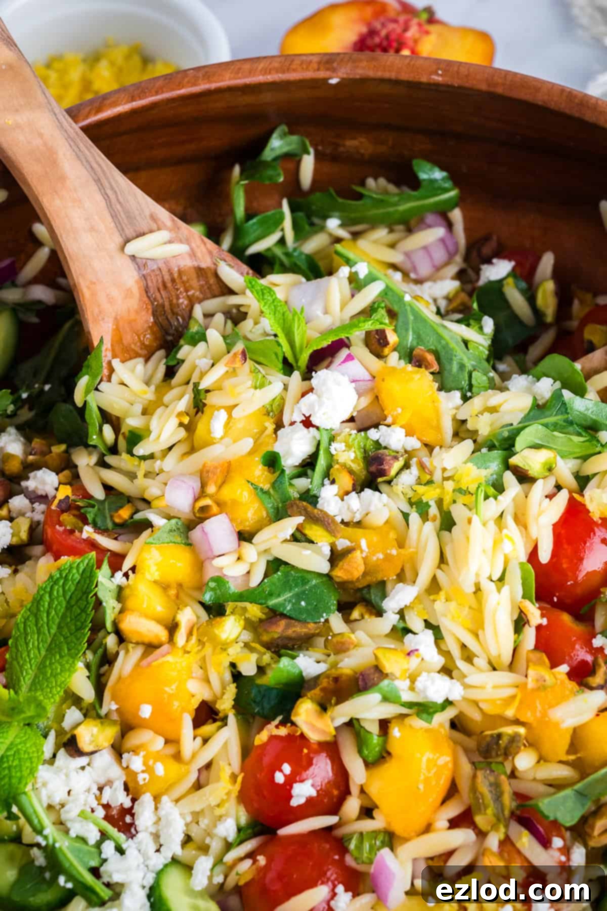 Spoon scooping orzo salad from a white bowl showing bright summer ingredients.