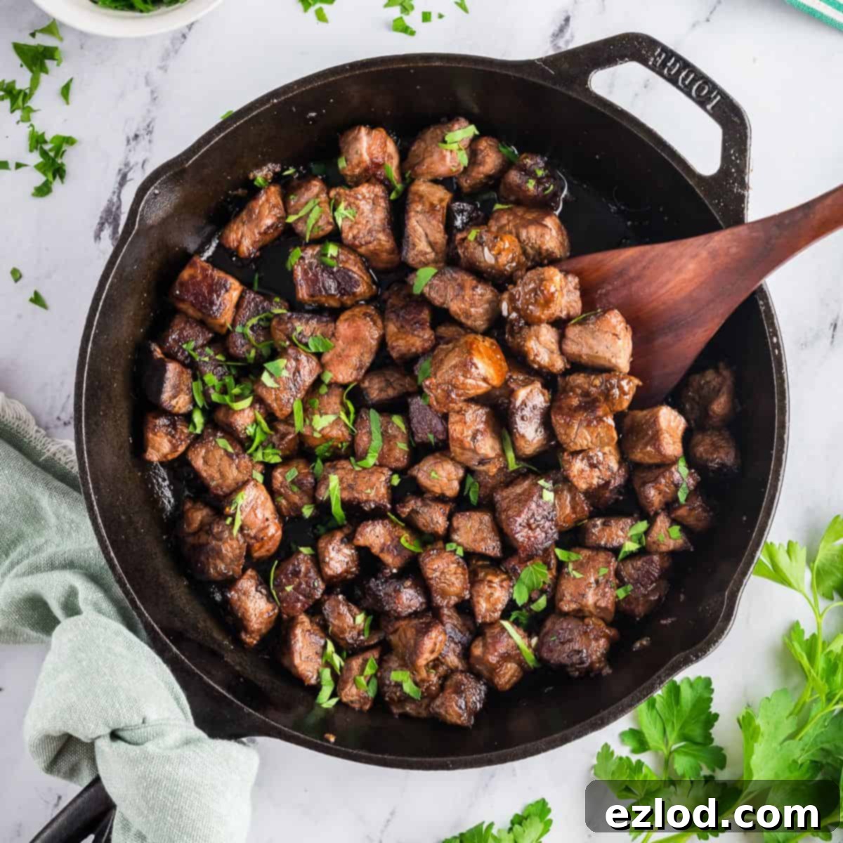 Cast-iron skillet with garlic butter steak bites garnished with fresh parsley.