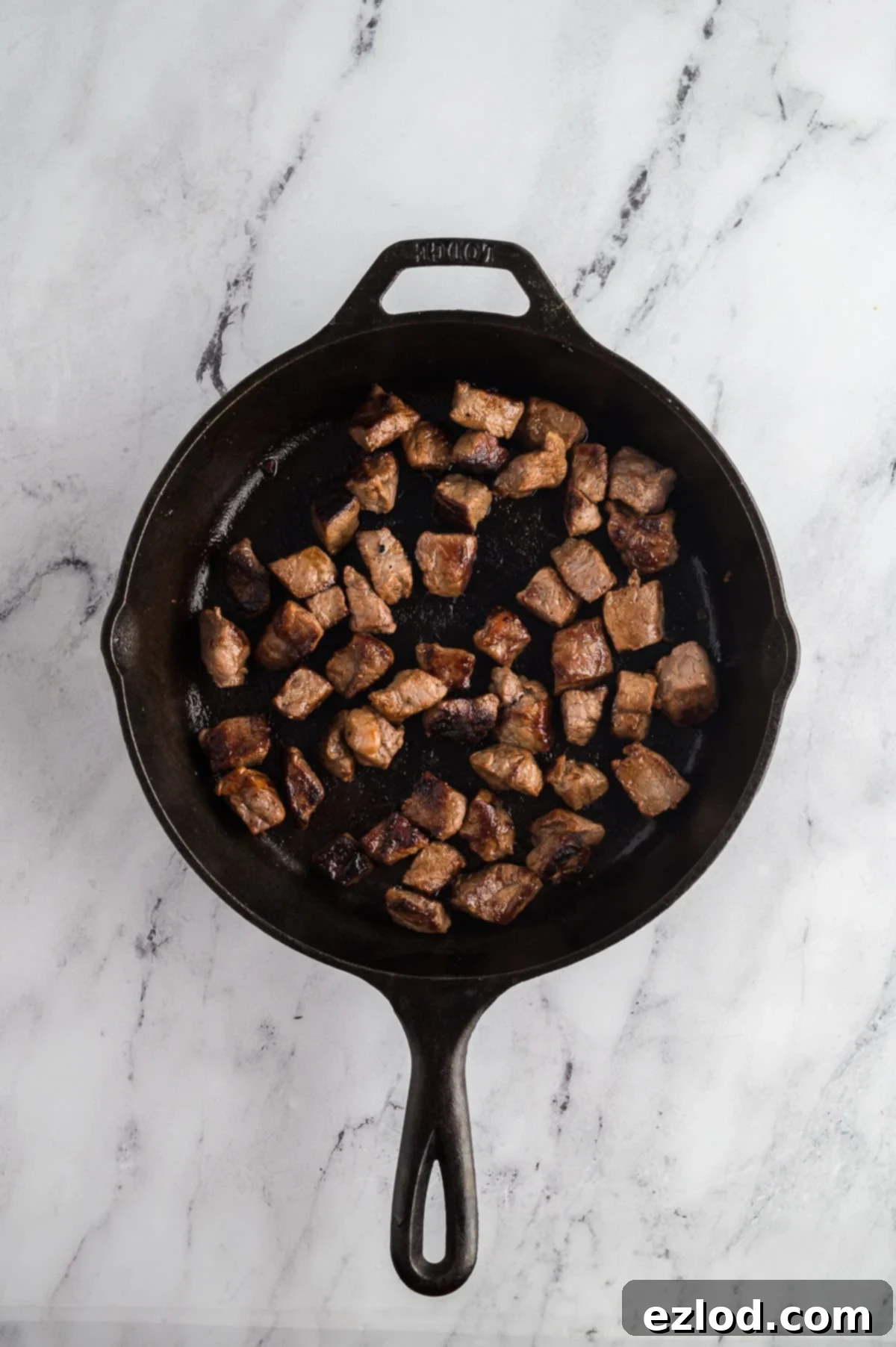 Steak bites being seared in a cast-iron pan.
