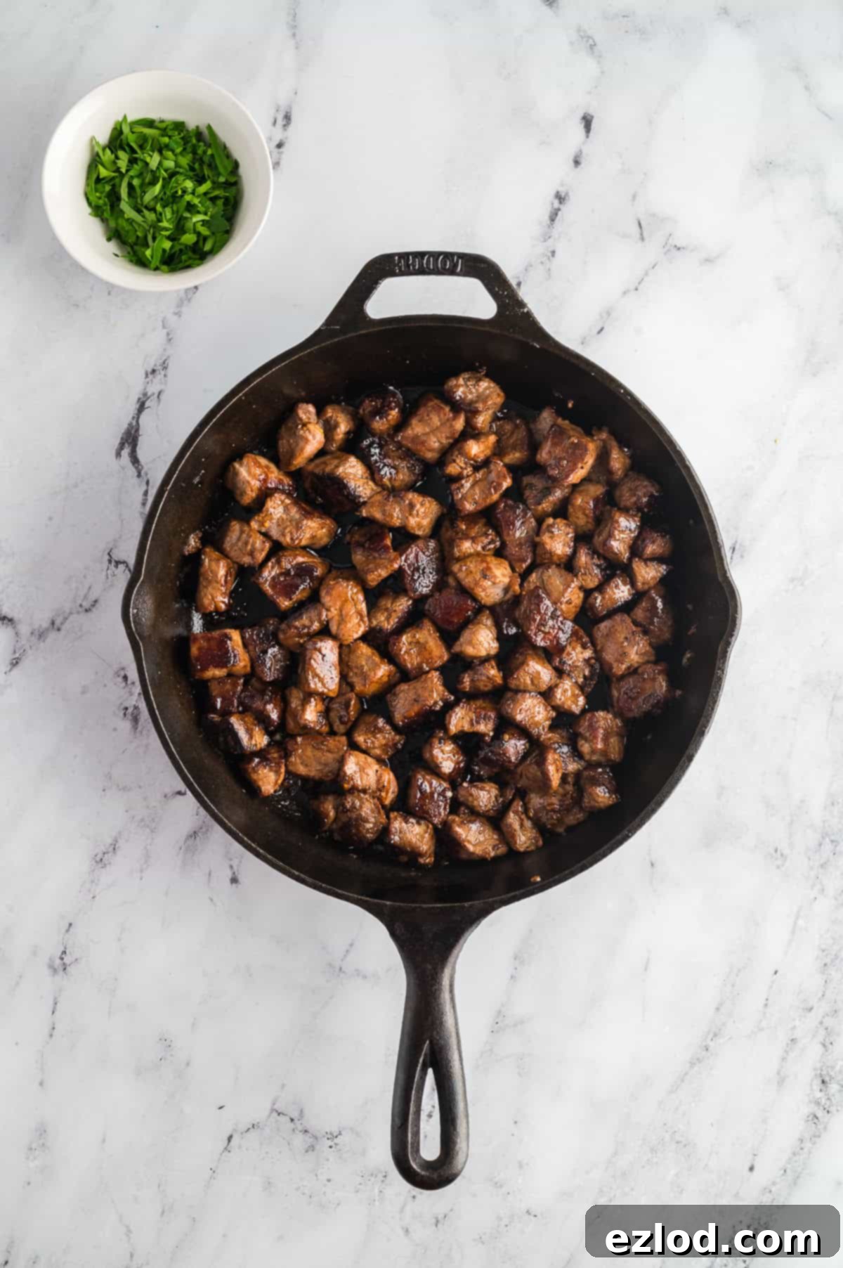 Steak bites coated in a buttery garlic sauce in a cast iron pan.