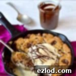 Top-down view of a freshly baked Nutella stuffed chocolate chunk skillet cookie, garnished with ice cream and extra chocolate drizzle.