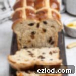 Sliced vegan hot cross bun loaf on a wooden board with a cup of tea and a bowl of butter.