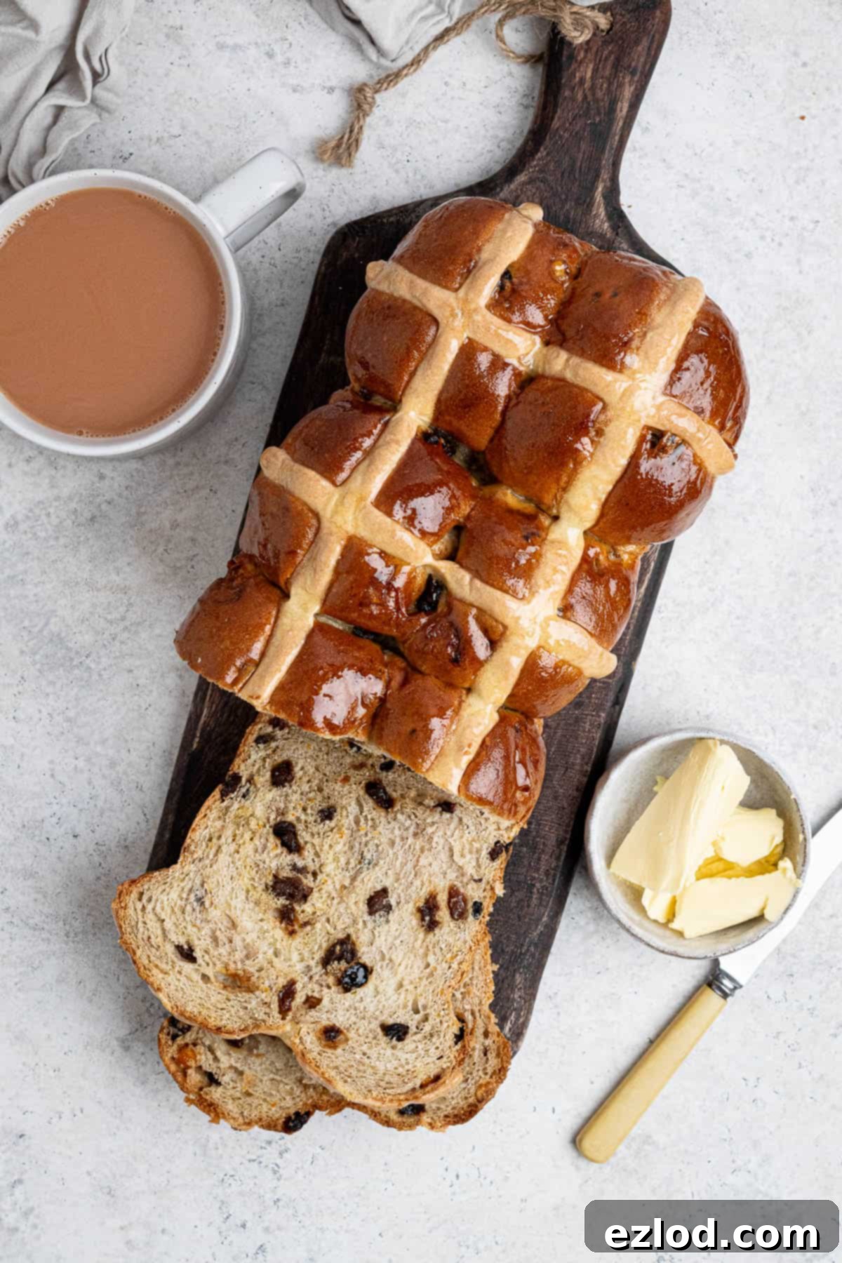 Top down shot of the vegan hot cross bun loaf on a wooden board with a cup of tea and bowl of butter.
