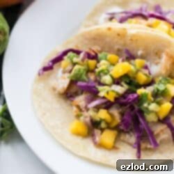Two Fish Tacos with Mango Salsa and red cabbage on corn tortillas on a white plate.