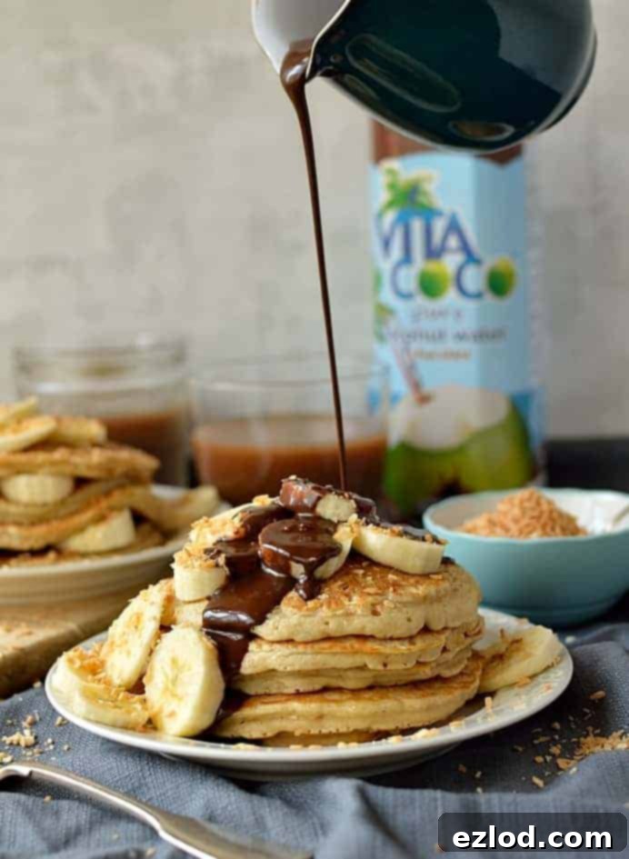 Toasted coconut pancakes with chocolate fudge sauce and banana, a decadent breakfast or brunch.
