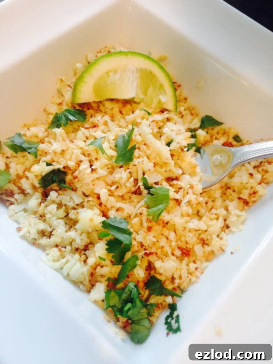 Cilantro lime cauliflower rice in a square bowl with a lime wedge and fork resting on the side