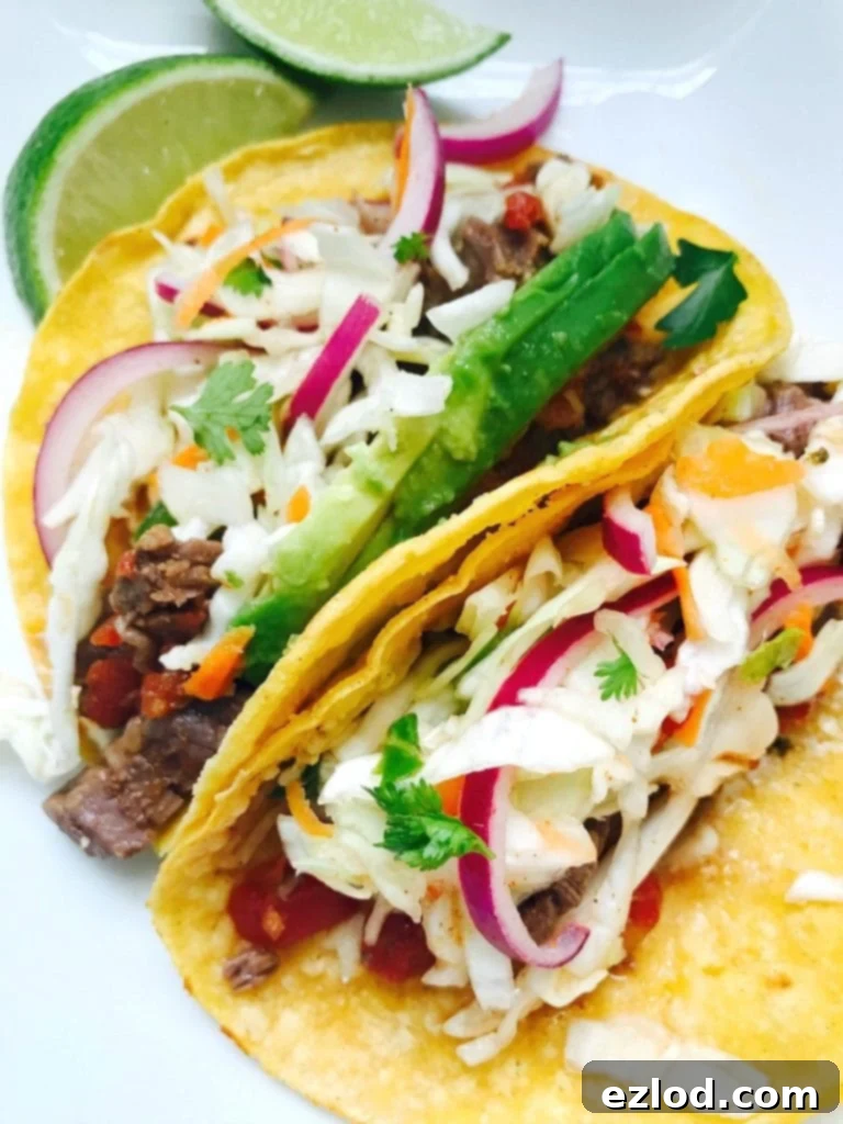 Tender Instant Pot Flank Steak Tacos 2 Two delicious Instant Pot Flank Steak Tacos with vibrant cilantro lime slaw, fresh cilantro, and avocado slices on a white plate with limes in the background.