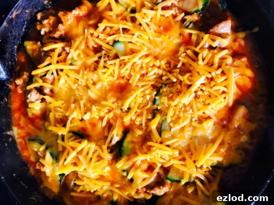 Cast Iron skillet filled with lean meat, zucchini, enchilada sauce, and topped with shredded cheddar cheese