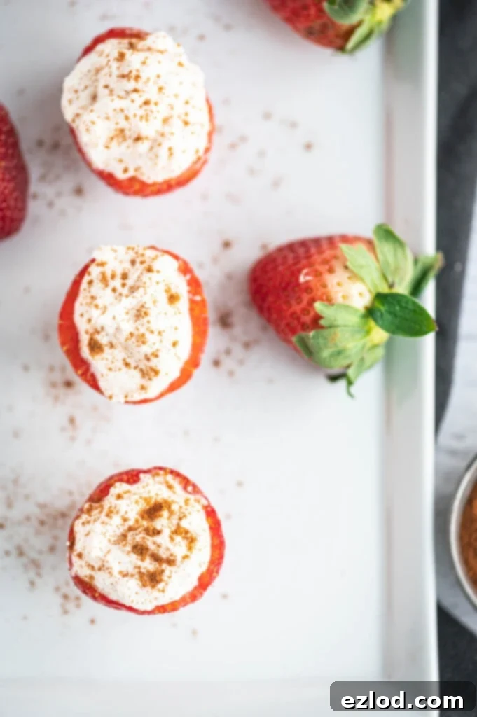 Overhead photo of cheesecake stuffed strawberries and whole strawberries on the side of a rectangular white serving dish.