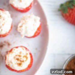 Overhead photo of Cheesecake Stuffed Strawberries with homemade whipped ricotta on a round white plate on a white wooden background.
