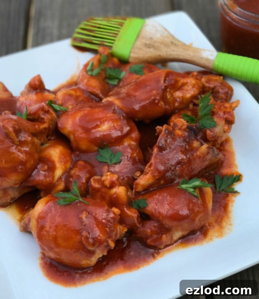 BBQ chicken thighs on a white plate with a green sauce brush on the side.