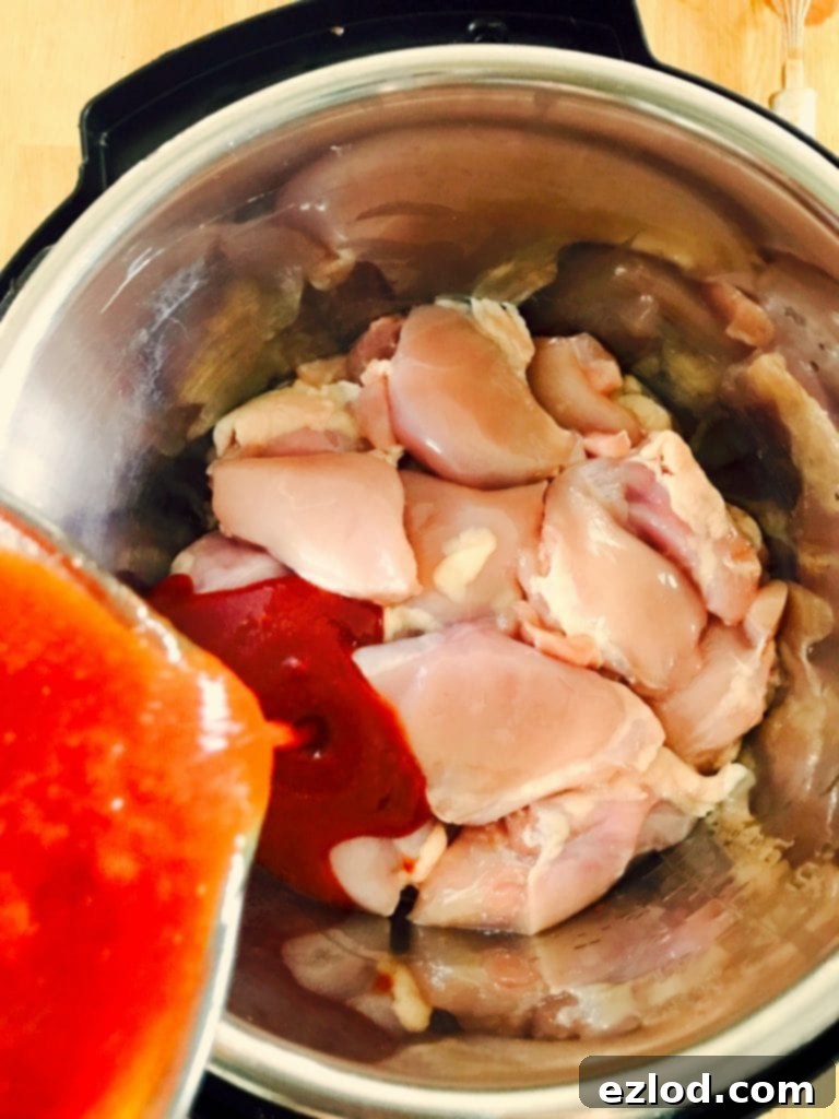 Raw chicken thighs in an instant pot with homemade bbq sauce being poured on top.