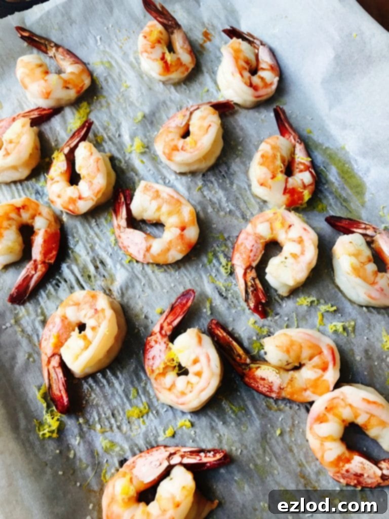 Roasted shrimp on a parchment lined sheet pan with lemon zest garnish