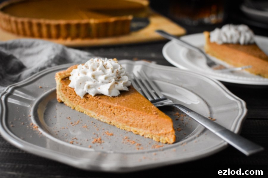 Slice of Pumpkin custard tart with whipped topping on gray plate with whole tart in the background
