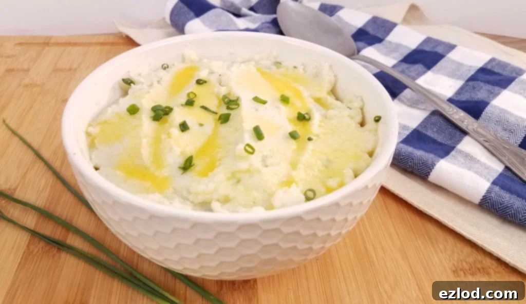 Whipped cauliflower mash in a white serving bowl with melted butter and chives on top.