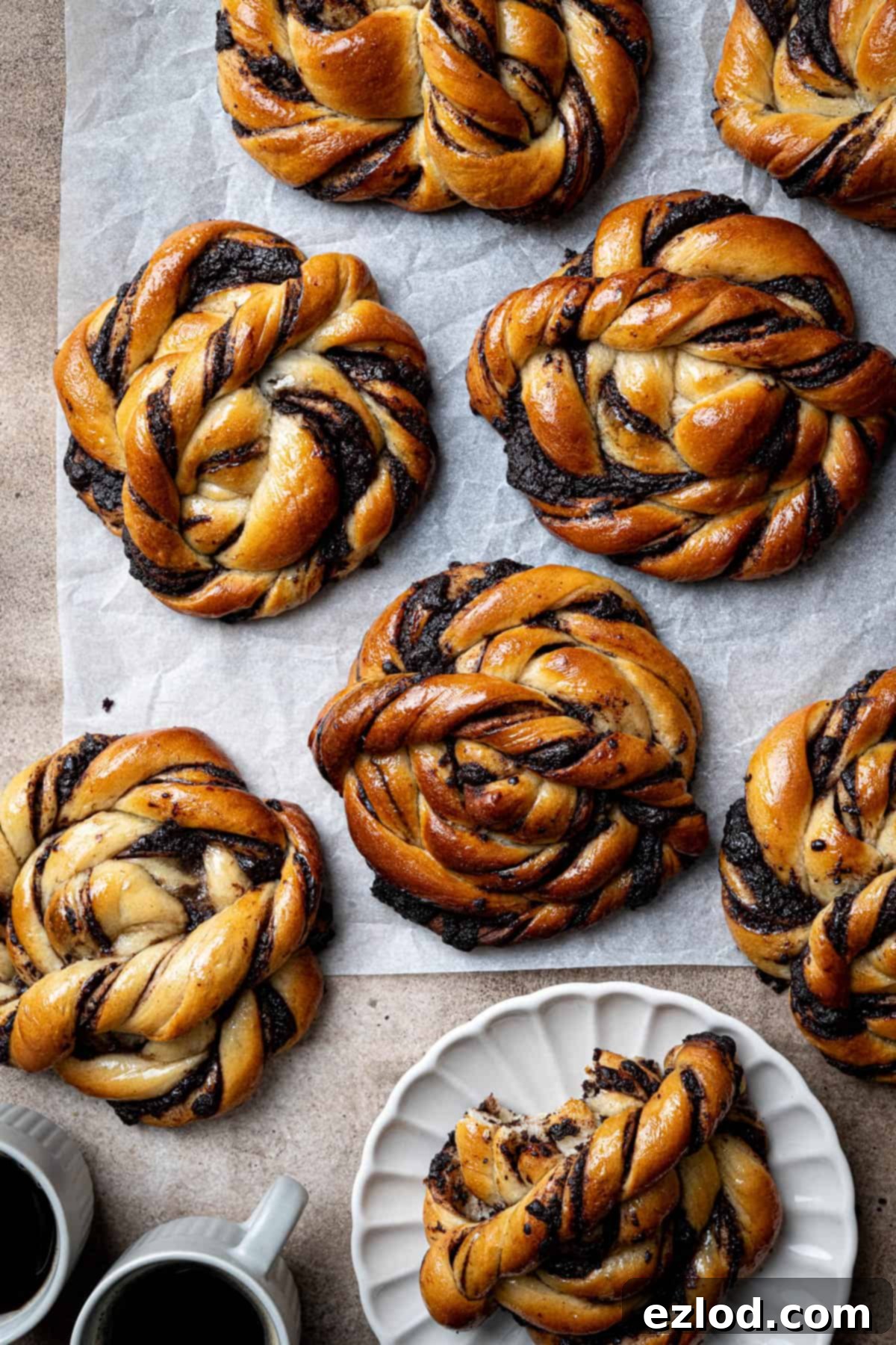 Vegan chocolate swirl buns on a sheet of baking paper, one on a plate with a bite taken out of it.