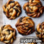 Vegan chocolate swirl buns on a sheet of baking paper, one on a plate with a bite taken out of it.