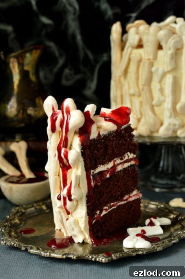 Overhead view of the Meringue Bone Graveyard Halloween Cake, featuring layers of chocolate, buttercream, and jam, topped with artfully arranged meringue bones and a splash of berry coulis