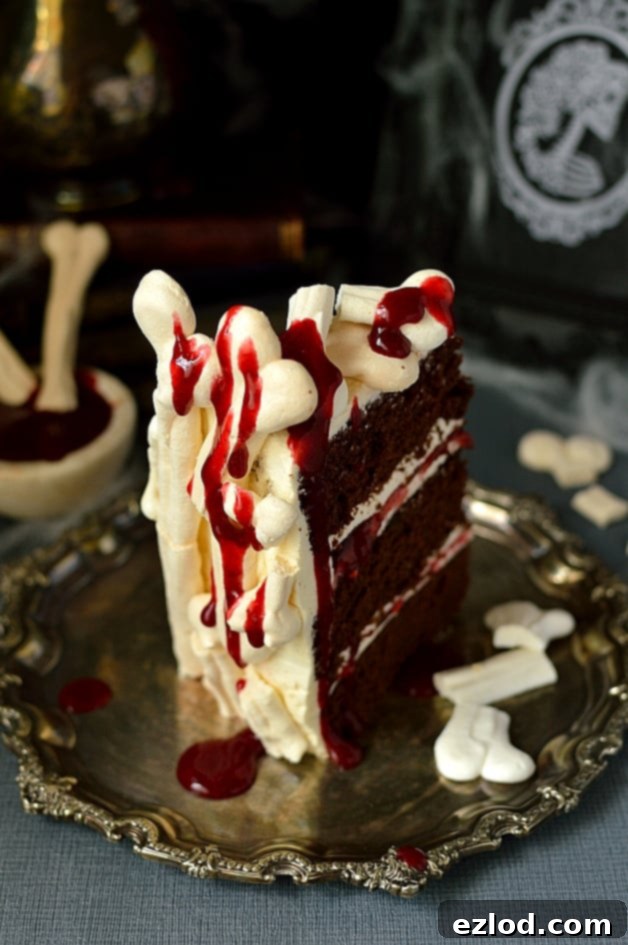 A slice of the Spooky Meringue Bone Palace Halloween Cake, revealing the moist chocolate cake layers, creamy vanilla Swiss meringue buttercream, and raspberry jam filling, adorned with meringue bones and berry coulis