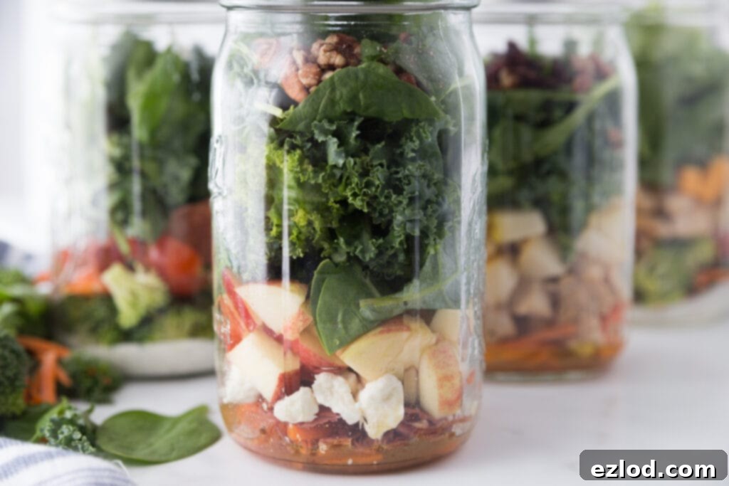 Two Fall Harvest Mason Jar Salads prepared side-by-side, showcasing vibrant layers of greens, fruits, proteins, and nuts. A perfect visual for healthy, make-ahead lunch ideas.