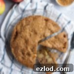 Simple wholemeal apple cake with two slices cut out on a blue and white cloth surrounded by apples and a bowl of sugar, a perfect visual for this easy vegan dessert.