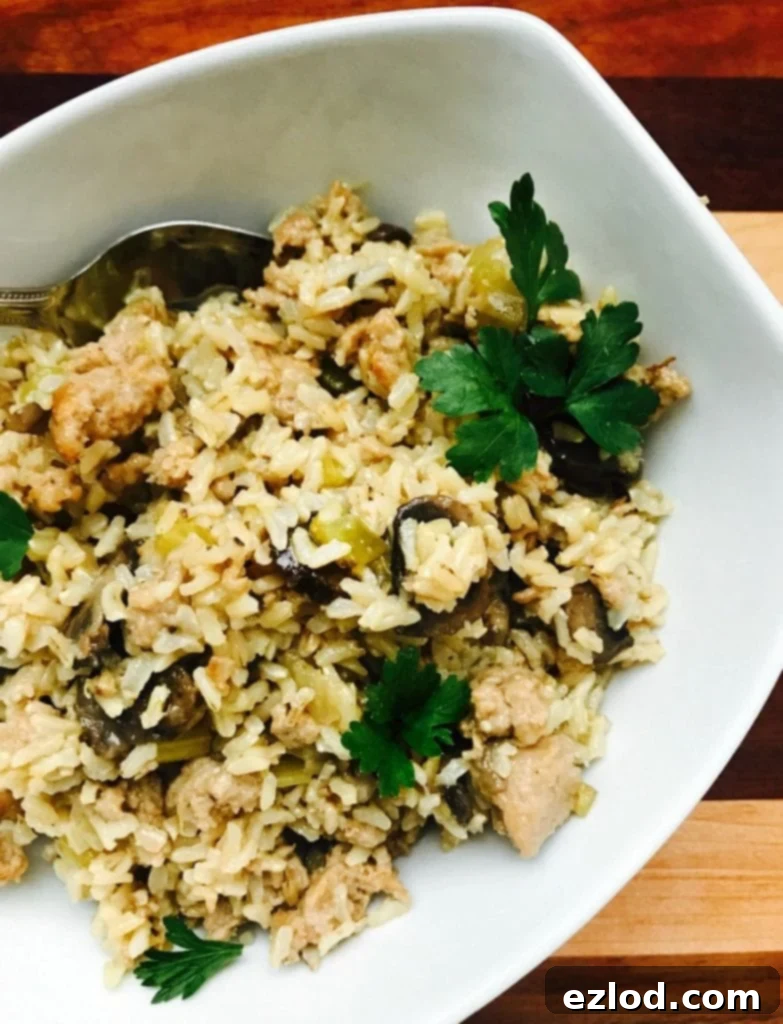 An overhead photo of a white rectangular bowl full of delicious, gluten-free Instant Pot Brown Rice and Sausage Stuffing, garnished with fresh herbs, ready to be served.