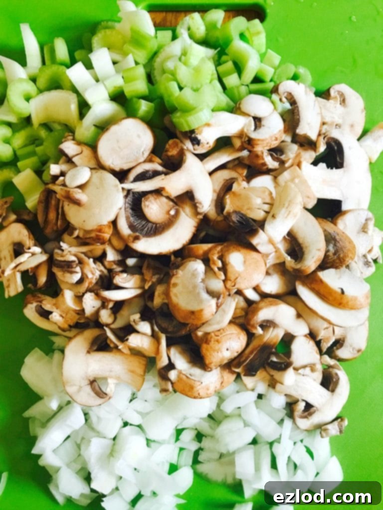 Raw diced celery, sliced mushrooms, and chopped onions on a vibrant green cutting board, perfectly prepped and ready to be sautéed.