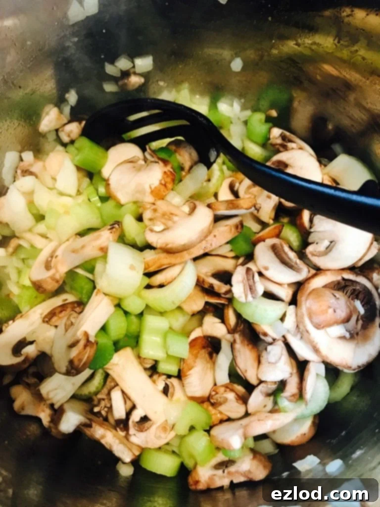 Raw celery, mushrooms, and onions sautéing in an Instant Pot with a black slotted spoon, preparing the flavorful base for the stuffing.