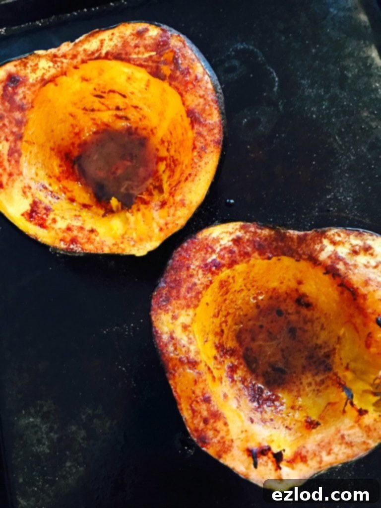An acorn squash is expertly cut in half and placed on a roasting pan. The interior of the squash shows a beautiful, caramelized brown color, indicating it's perfectly roasted and tender.