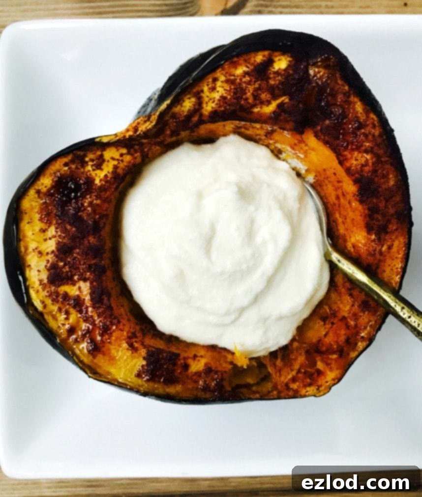 A close-up view of a perfectly roasted acorn squash half, its edges slightly browned and caramelized, forming a natural heart-like shape on a white plate. It's generously filled with the creamy, sweet whipped ricotta.