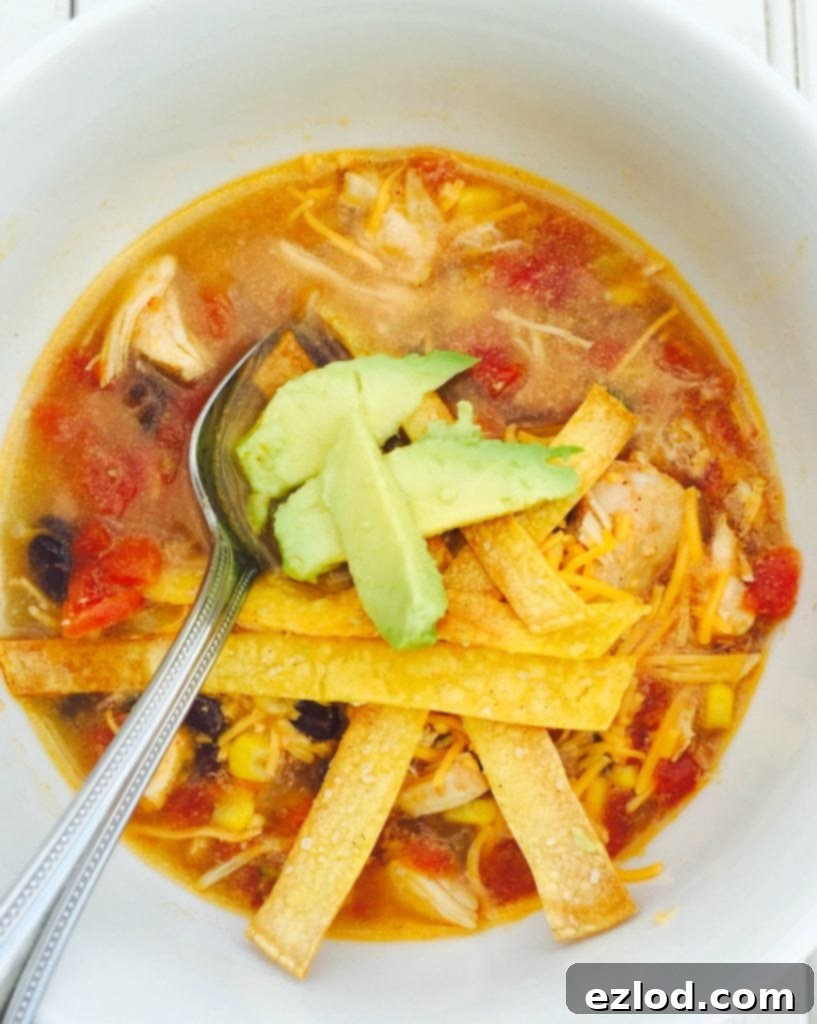 Close up photo of a bowl of chicken tortilla soup topped with diced avocado and homemade tortilla strips.