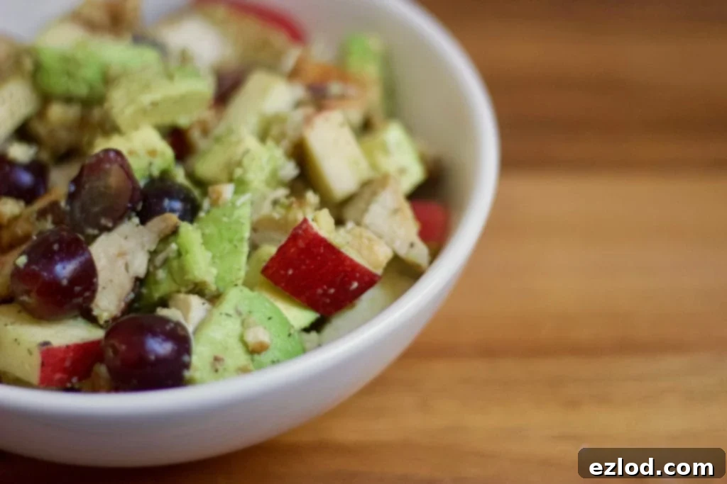 Mixed 21 Day Fix Avocado Chicken Salad, with diced chicken, grapes, walnuts, apples, and avocado, in a white bowl on a wooden surface.