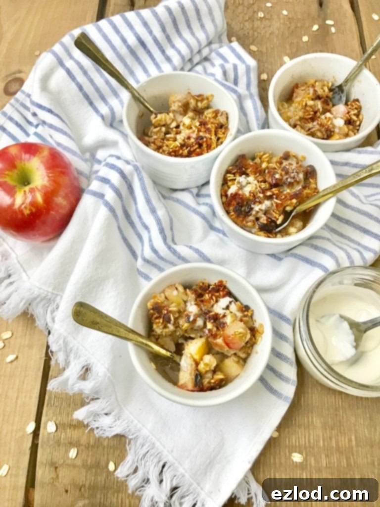 Four white ramekins of Instant Pot apple crisp sitting on a wooden background with coconut cream and an apple sitting nearby 