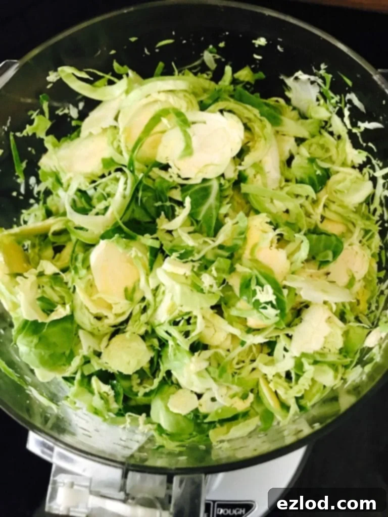 Overhead view of shaved Brussels sprouts in a food processor with the lid off.
