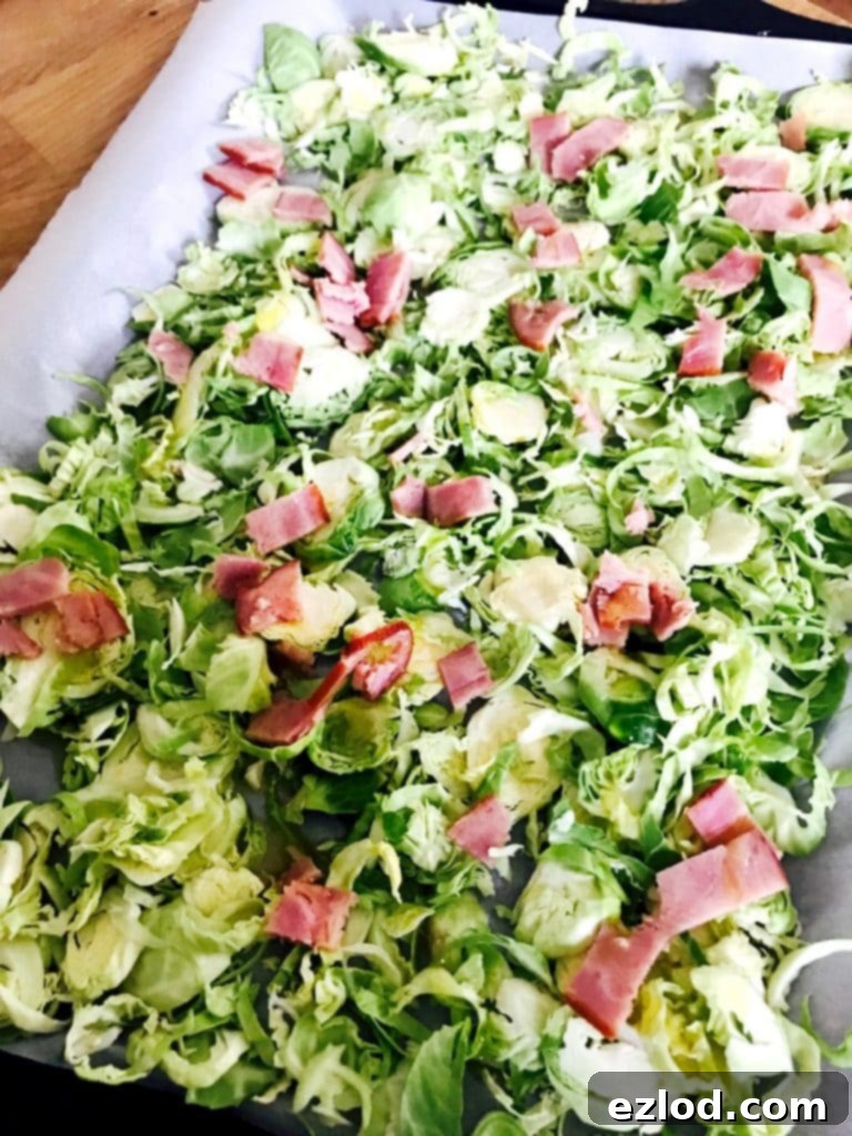 A sheet pan full of uncooked shaved Brussels sprouts and diced turkey bacon.