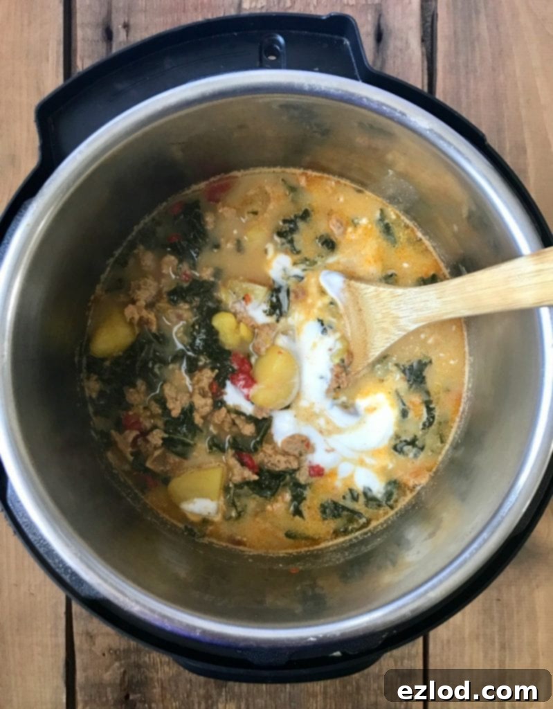 A large pot of healthy Zuppa Toscana simmering on the stove, filled with chicken sausage, potatoes, kale, and roasted red peppers.