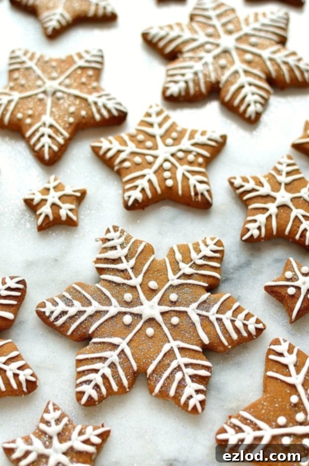 Beautifully decorated gingerbread star and snowflake cookies, adorned with white royal icing patterns.