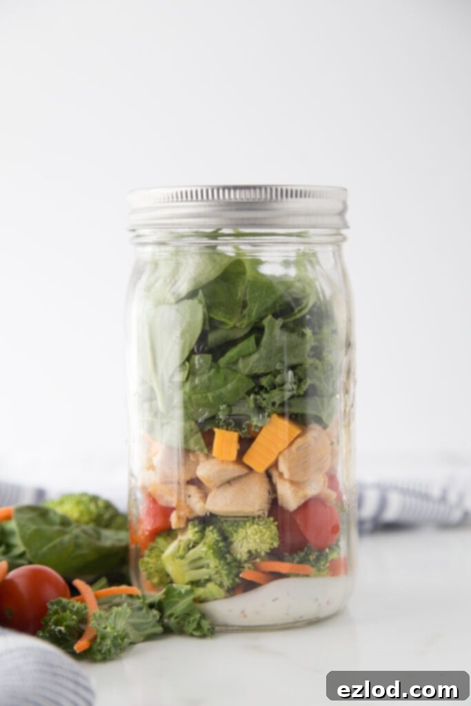 A Jar of BLT Mason Jar Salad with homemade ranch dressing, carrots, broccoli, tomatoes, and leafy greens, ready for meal prep.