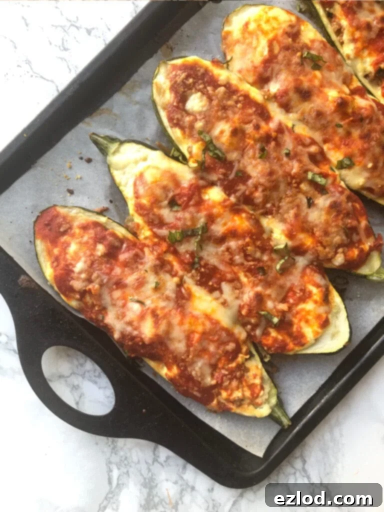 Baking sheet with Lasagna Stuffed Zucchini Boats on a marble backdrop. Boats have been broiled and the cheese is bubbly and crispy. This image perfectly showcases the golden, bubbly, and melty cheese topping on our delicious low carb zucchini boats, fresh out of the oven, highlighting the perfect texture and tempting appeal of the dish.