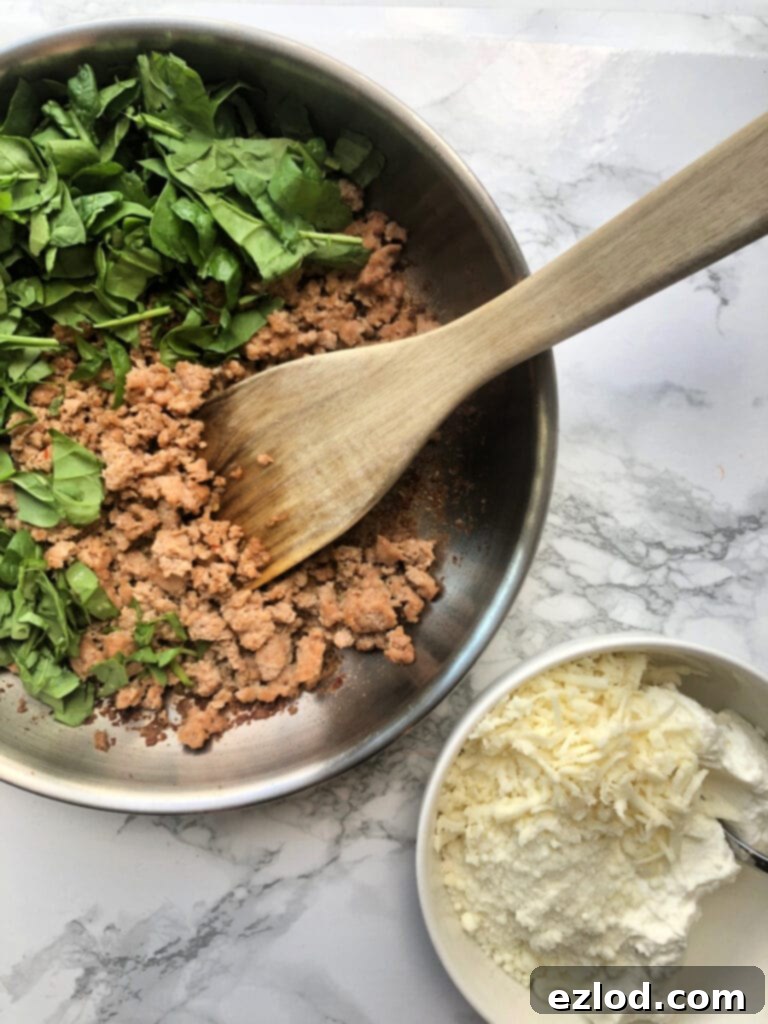 A pan with sautéed vegetables and chicken sausage, forming the savory lasagna stuffing for Zucchini Lasagna Boats. Beside it, a bowl holds a creamy blend of ricotta, parmesan, and mozzarella cheese, ready to layer and create a rich, comforting filling.