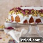 Vegan Persian love cake topped with pistachios and rose petals on a glass cake stand.