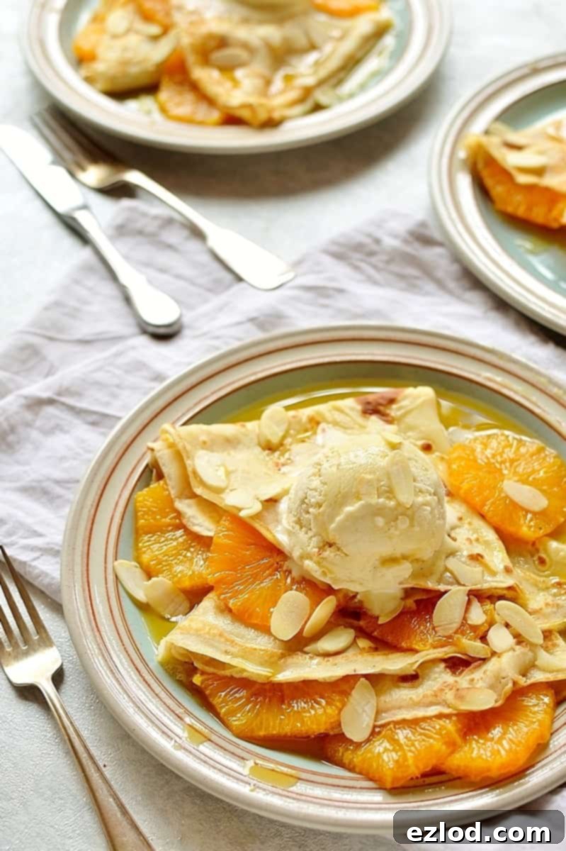 Close-up of a stack of golden crepes with caramel orange slices, ready for a scoop of almond ice cream.
