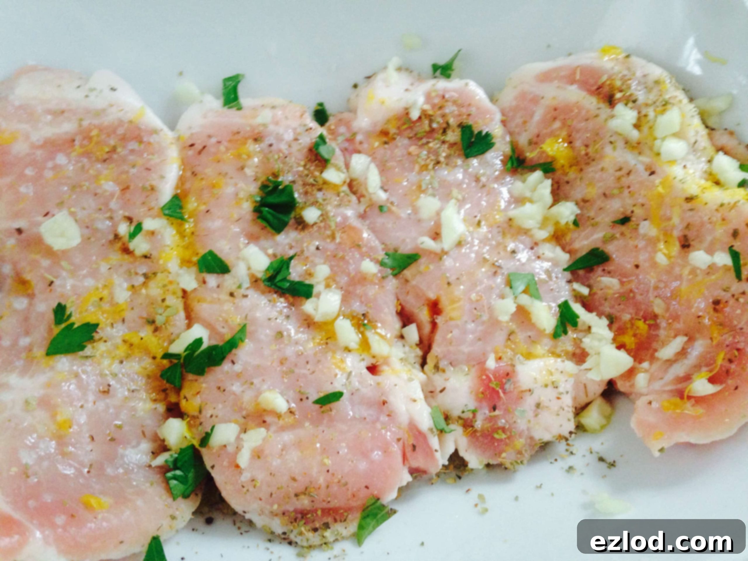 Uncooked pork chops marinating in lemon and herbs