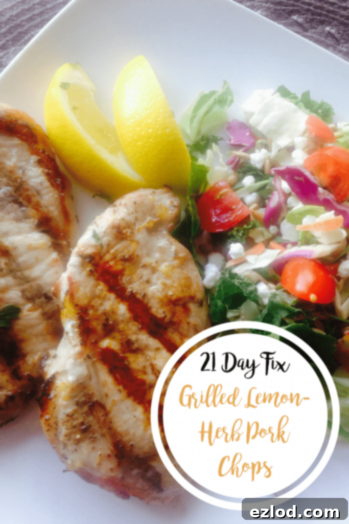 Two Grilled Lemon-Herb Pork Chops next to a side salad and lemon wedges on a square white plate with the text overlay- 21 Day Fix Grilled Lemon-Herb Pork Chops