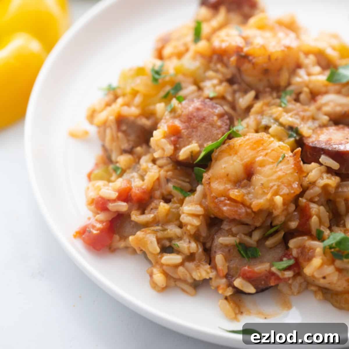 A white plate with healthy Instant Pot Jambalaya featuring brown rice, shrimp, colorful peppers, and chicken sausage.
