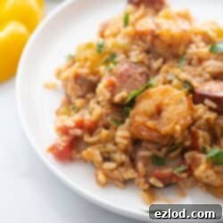 A white plate with healthy Instant Pot Jambalaya featuring brown rice, shrimp, colorful peppers, and chicken sausage.
