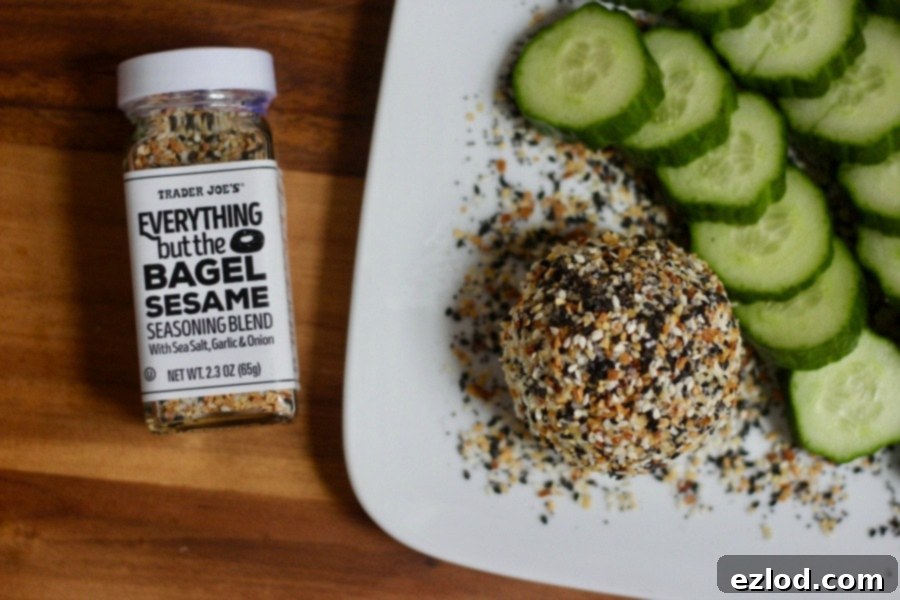 Everything Bagel Goat Cheese rolled in seasoning, served with fresh cucumber slices on a wooden board. A perfect healthy snack.