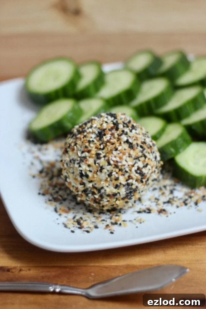Close-up of Everything Bagel Goat Cheese balls, one bitten, showing the creamy texture and seasoning, alongside fresh cucumber slices.